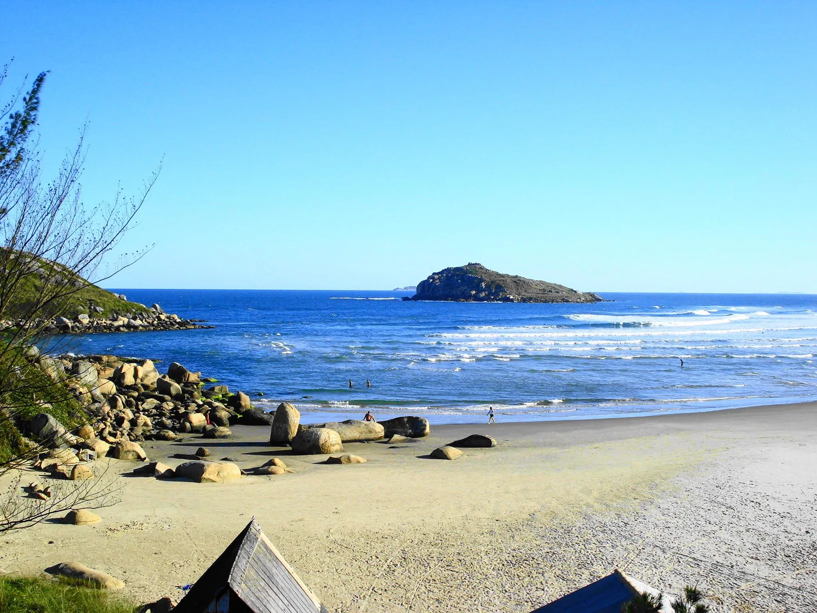 A Praia da Vila desde o canto de pedras, com a Ilha Santana recortada no horizonte e a ondulação entrando limpa ao longo da areia.