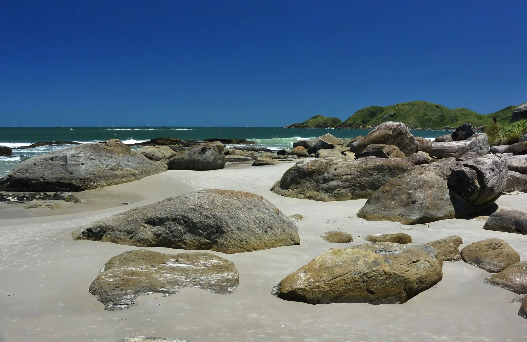 Os blocos de pedra espalhados pela areia branca da Praia Grande, com os morros de mata fechando o canto ao fundo.
